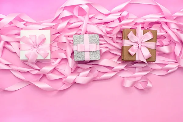 Tres cajas con regalos en el fondo de la revolución de cintas decorativas de satén de color rosa . — Foto de Stock