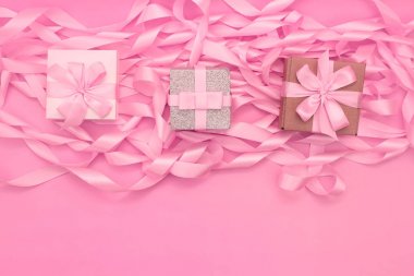 Arka planda hediyeler ile üç kutu pembe renkli dekoratif saten kurdela devrim.