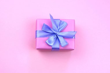 Dekoratif şenlikli hediye kutusu ile pembe renk pembe bir arka plan üzerinde. Lila saten şerit yay.