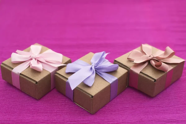 Feestelijke samenstelling drie Kraft dozen met giften op helder roze achtergrond. — Stockfoto