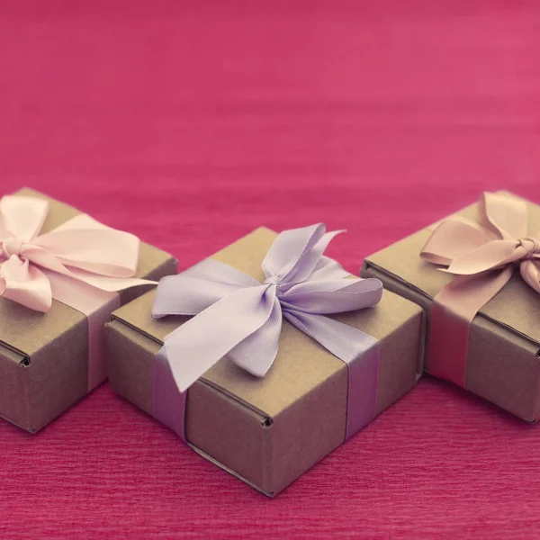 Εορταστική σύνθεση τριών Κραφτ κουτιά με δώρα σε φωτεινά ροζ φόντο. — Φωτογραφία Αρχείου