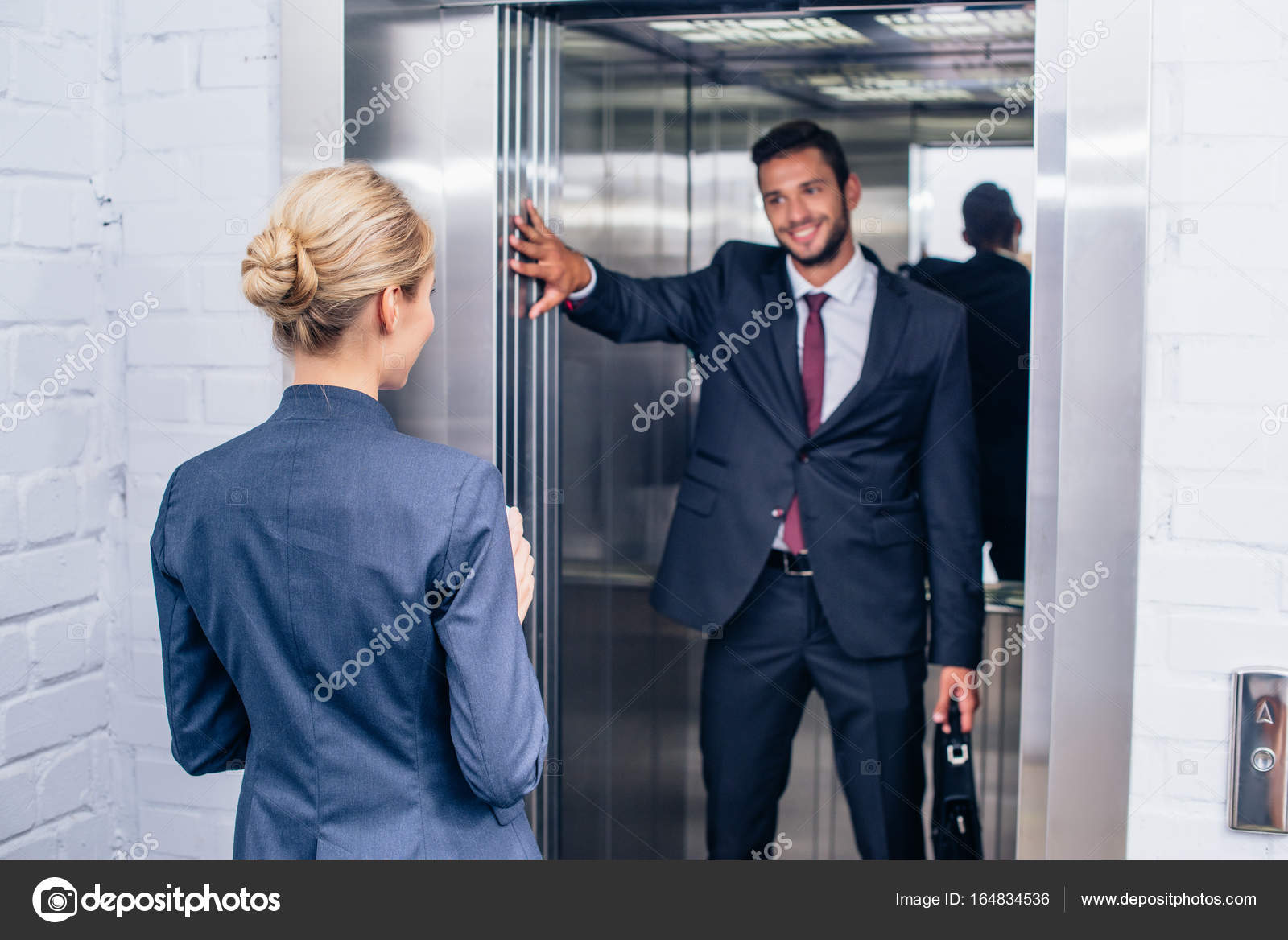 Businessman holding elevator door for woman Stock Photo by