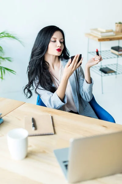 Businesswoman applying lipstick at workplace — Stock Photo, Image