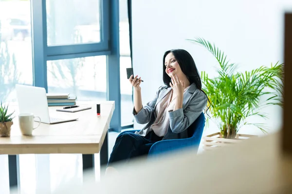 Businesswoman applying lipstick at workplace — Stock Photo, Image