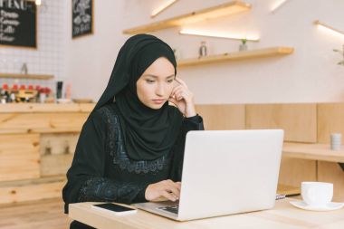 muslim woman using laptop in cafe clipart