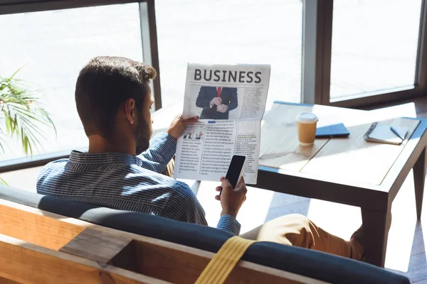 Man with smartphone reading newspaper — Stock Photo, Image