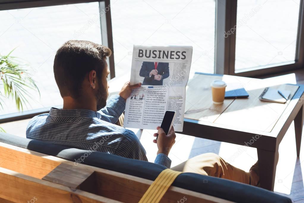 man with smartphone reading newspaper