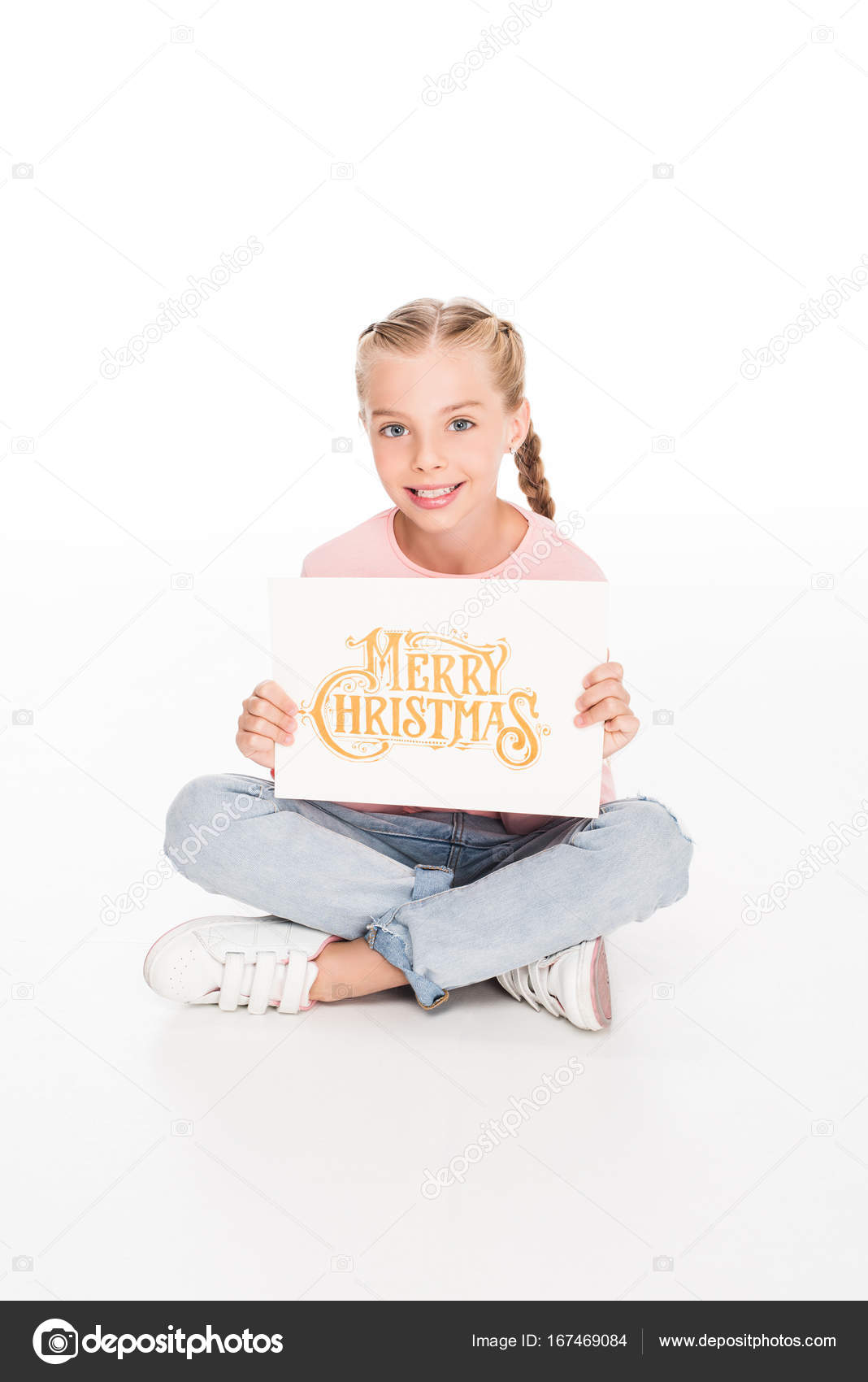 bambino con la cartolina di buon Natale — Foto Stock Bambino sorridente che si siede sul pavimento con le gambe incrociate e mostrando la tessera con testo buon Natale su di esso isolato su bianco — Foto di
