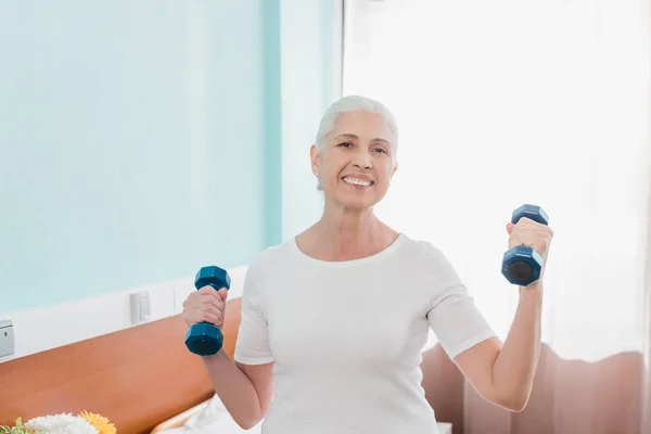 Senior woman with dumbbells in hospital — Stock Photo, Image