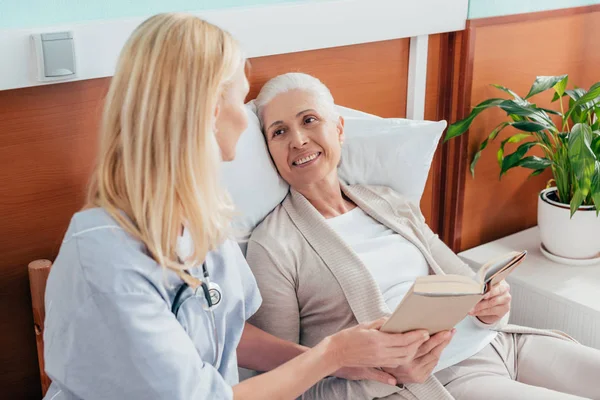 Verpleegkundige en senior patiënt met boek — Stockfoto