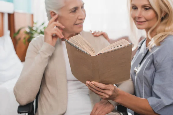 Infermiere e paziente anziano con libro — Foto Stock