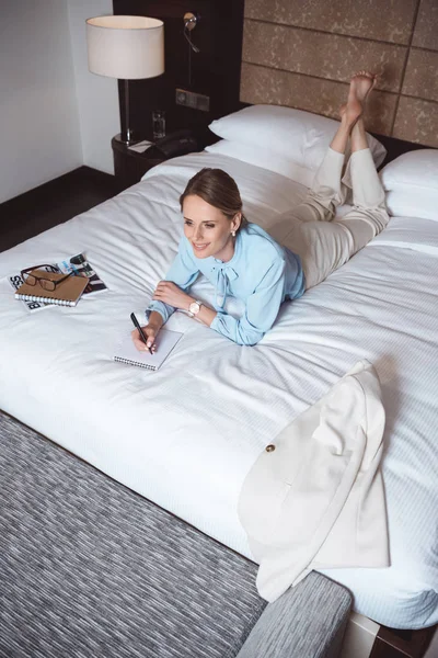 Businesswoman writing in notebook on bed — Free Stock Photo