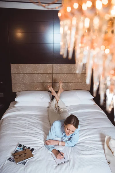 Businesswoman writing in notebook on bed — Stock Photo, Image