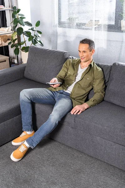 Man with tv remote sitting on couch — Stock Photo, Image