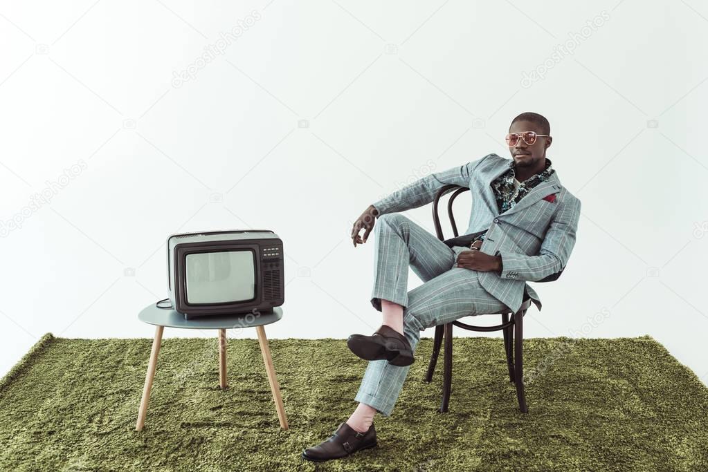 man in sunglasses and suit on chair with tv