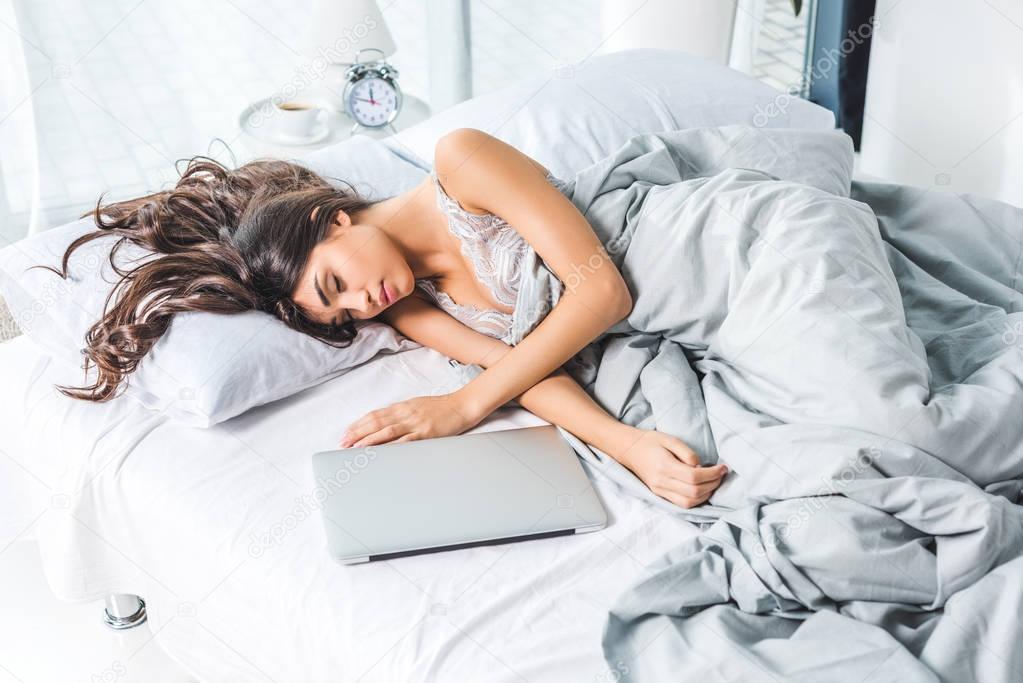 Beautiful brunette girl sleeping on bed with laptop