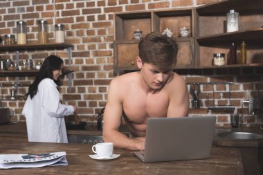 man using laptop while girlfriend cooking clipart