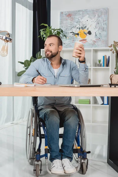 Человек на инвалидной коляске сидит за рабочим столом — стоковое фото