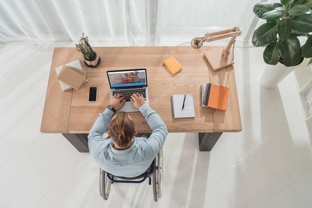 Top view of disabled man on wheelchair using laptop at workplace