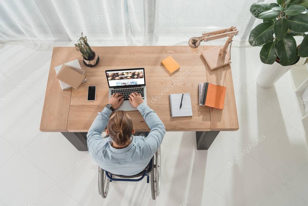 Top view of disabled man on wheelchair using laptop at workplace