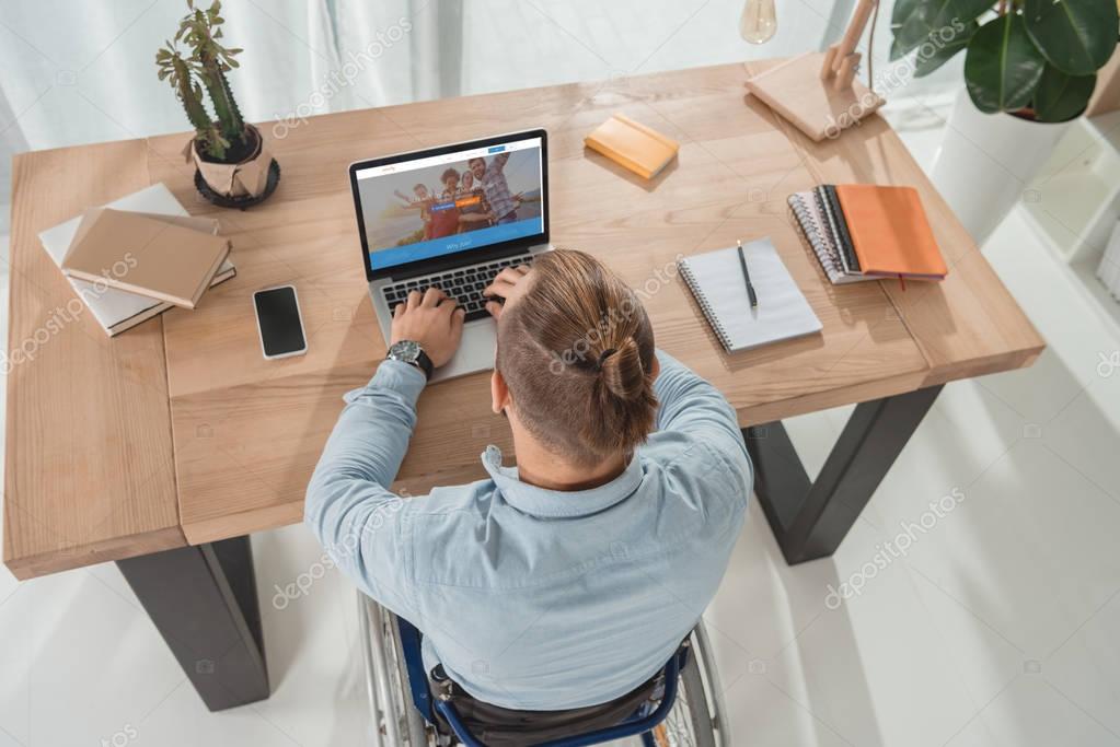 High angle view of disabled man on wheelchair using laptop at workplace