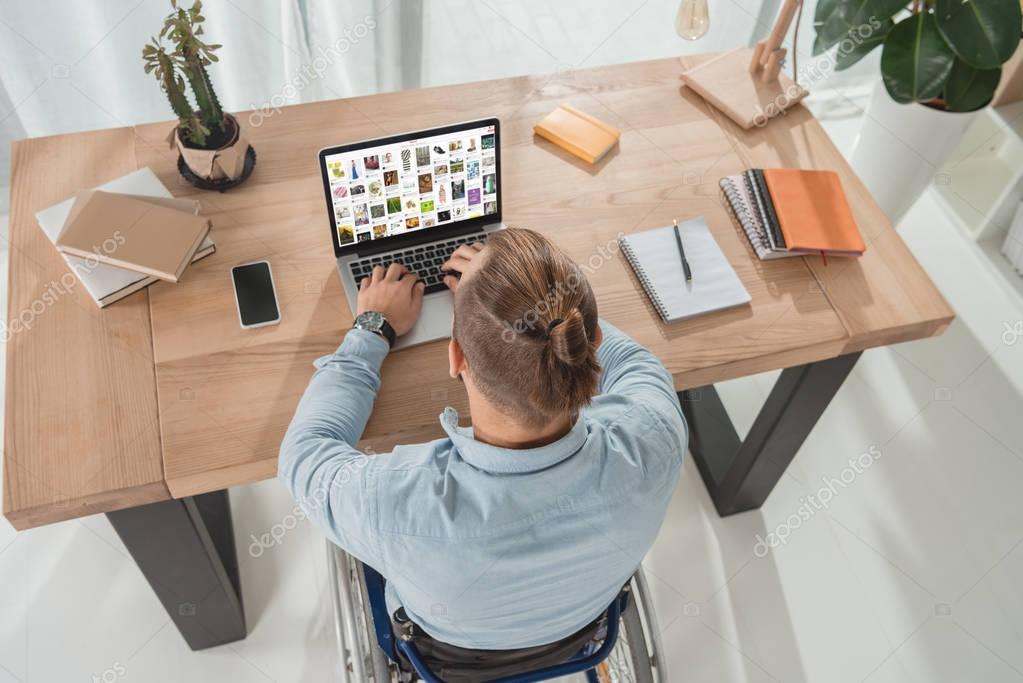 High angle view of disabled man on wheelchair using laptop with pinterest website