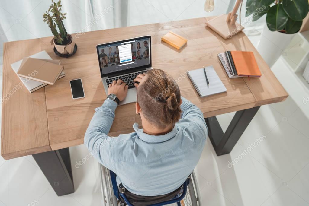 High angle view of disabled man on wheelchair using laptop with linkedin website
