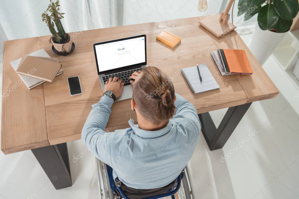 High angle view of disabled man on wheelchair using laptop with google website