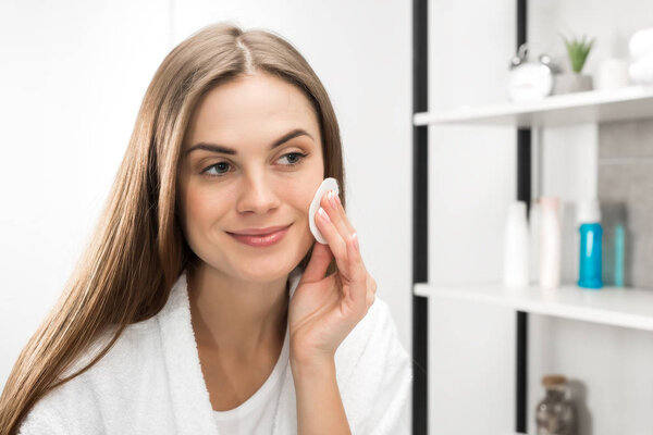 Woman cleaning face with cotton pad