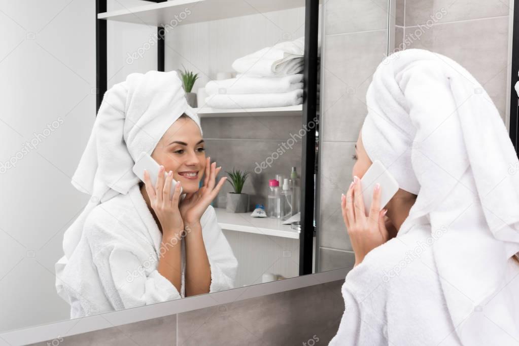 Woman talking by smartphone and checking skin