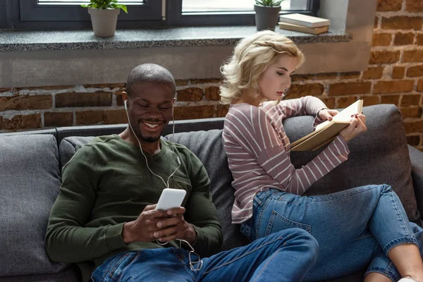 Smiling African American Man Listening Music While Caucasian Girlfriend Reading — Free Stock Photo