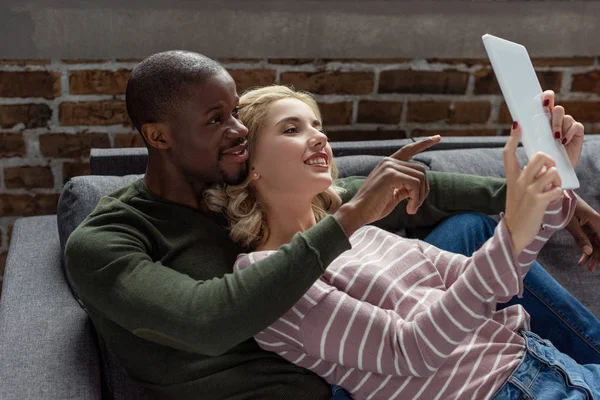 Retrato Sonriente Pareja Multicultural Usando Tableta Juntos Mientras Descansan Sofá — Foto de Stock