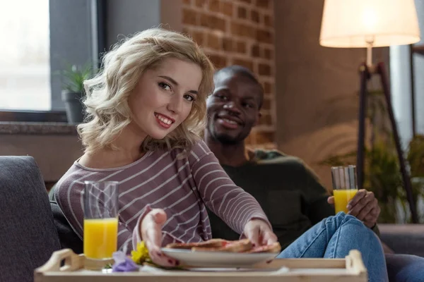 家で一緒に朝食を持っている多文化の若いカップルの笑顔の選択と集中  — 無料ストックフォト