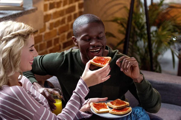 Glückliche Frau Füttert Afrikanisch Amerikanischen Freund Mit Toast Beim Frühstück — Stockfoto