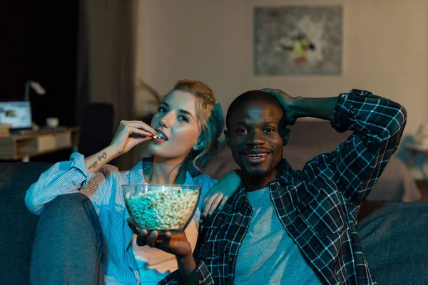 ポップコーンを食べたり 自宅のソファーに一緒に映画を見て多民族のカップルの肖像画 — ストック写真