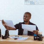 Ritratto di fotografo afroamericano concentrato che guarda esempi di fotoshooting sul posto di lavoro