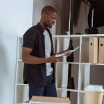 Vue de côté du photographe afro-américain focalisé regardant les papiers dans les mains en studio