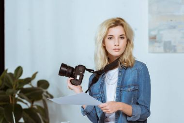 portrait of young photographer with photo camera and photoshoot example looking at camera in studio clipart