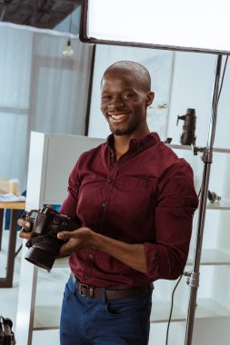 kamera Studio bakarak elinde fotoğraf makinesi ile neşeli Afrikalı-Amerikalı fotoğrafçı portresi