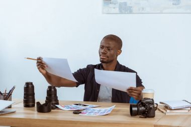 portrait of focused african american photographer looking at photoshoot examples at workplace clipart