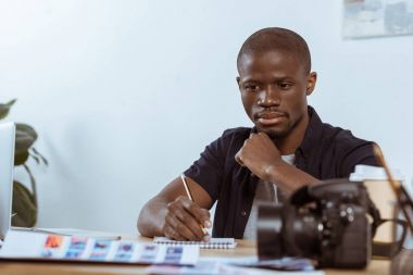 portrait of pensive african american photographer working at workplace in office clipart