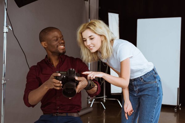 african american photographer and caucasian model choosing photos together during photoshoot in studio