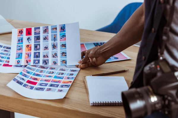 partial view of african american photographer holding photoshoot examples at workplace in office