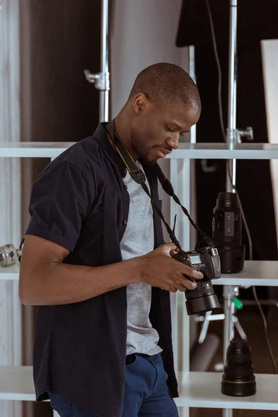 スタジオで写真をカメラ上で写真を選択するアフリカ系アメリカ人の写真家の側面図  — 無料ストックフォト