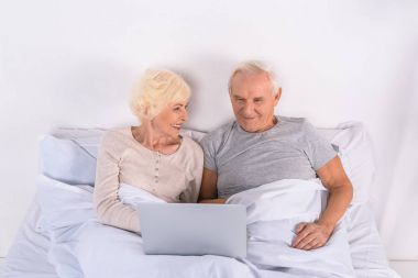 üst düzey çift evde yatakta istirahat ederken dizüstü bilgisayar kullanarak