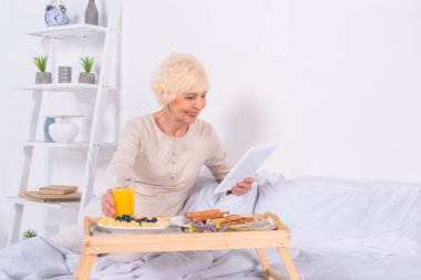 kadın evde tablet kullanarak yatakta kahvaltı ile kıdemli mutlu