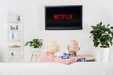 back view of senior couple watching netflix on tv at home clipart