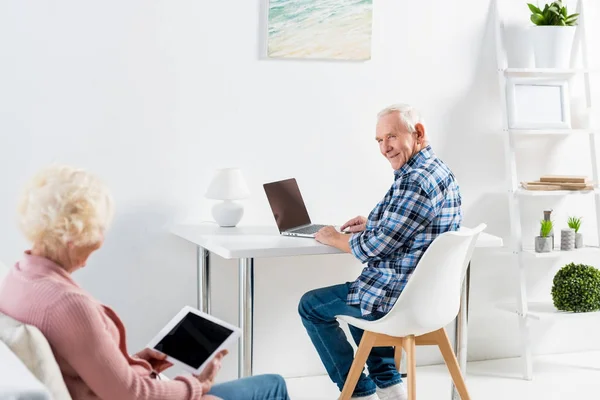 自宅のソファーに座っていた妻を見てノート パソコンとテーブルで年配の男性の部分的なビュー — ストック写真