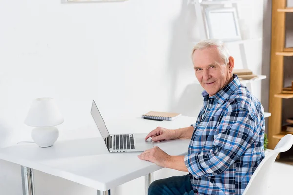 坐在桌上的老人的侧面看着笔记本电脑 在家里看摄像头 — 免费的图库照片