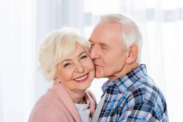 portrait of senior man kissing happy wife that looking at camera